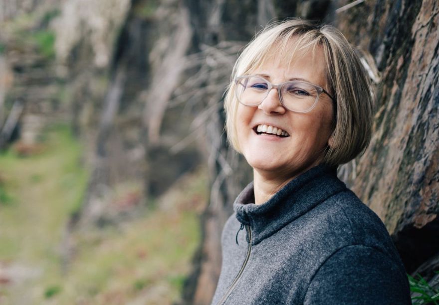 Susanne Barth lachend an einer Mauer lehnend in den Weinbergen